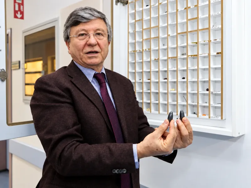 Prof. Dr. Mustafa Melikoğlu koleksiyon vitrininin önünde iki yabancı cisim örneğini gösteriyor